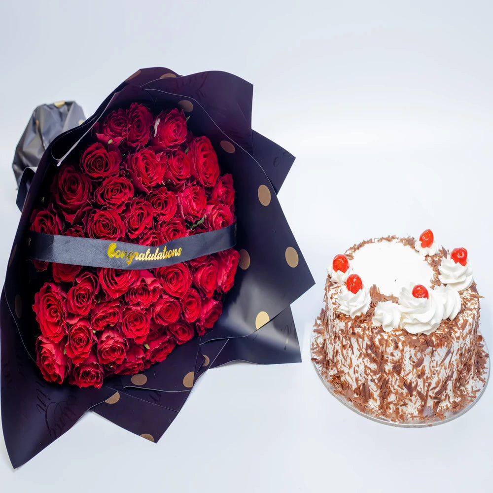 Premium red roses with congratulatory ribbon and celebration cake, arranged by Zuri Blooms