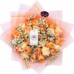 Bouquet of orange and beige roses with baby's breath on pink paper, featuring Zuri Flowers brand.